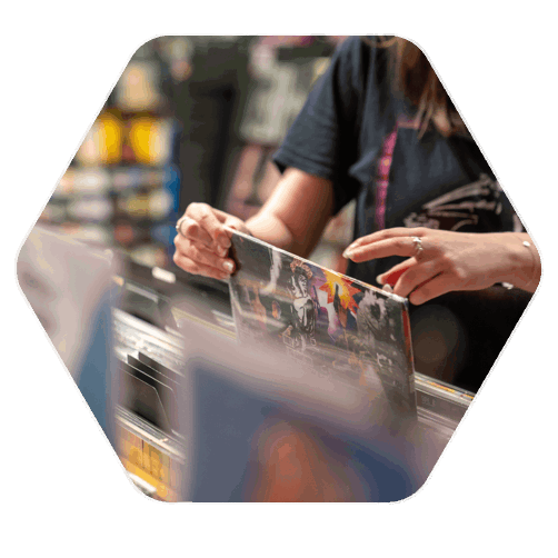 A ladies hands picking up a vinyl cover in a market stall where there are many vinyl's lined up together in a stacked formation