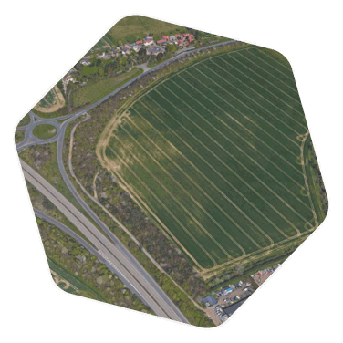 An aerial shot of a large green field with rounded lines where a tractor has left spaces in the field, the field is next to a main road with two lanes