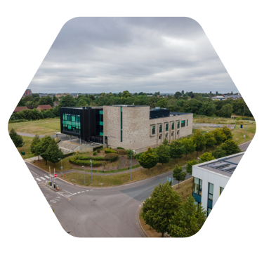 An arial shot of the Anglia Ruskin medical building which is a large modern building set back from a private road, surrounded by planted trees and some small field areas