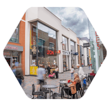 A busy Bond Street, which is a high street in Chelmsford. There a modern shops situated on the street and people are blurred in the image, moving and walking through the street.