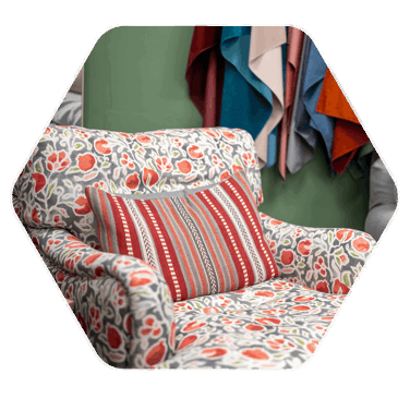 A vibrant, patterned armchair in a grey, red and green floral design with a striped cushion sat upright on the armchair 