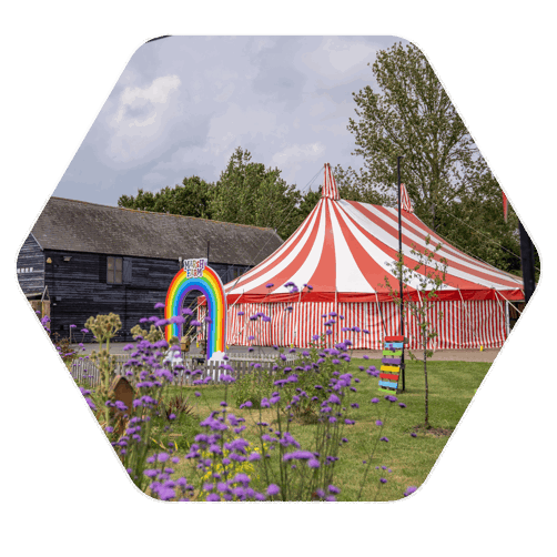 An outside space on a sunny day with a large red and white striped marquee sat in the middle of the picture with a rainbow style entrance, arched doorway that reads "Marsh Farm"