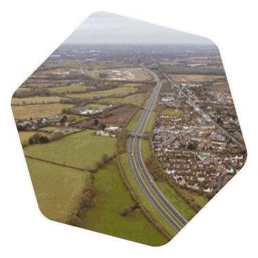 A drone shot of fields and a motorway with some houses set back from the road, the drone shot is taken above the Great Leighs area