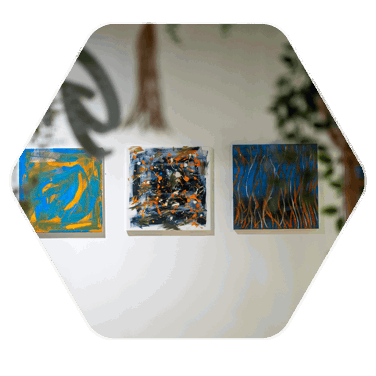 Three canvas paintings hanging on a plain white wall. The paintings contain bright colours and large streaks of paint