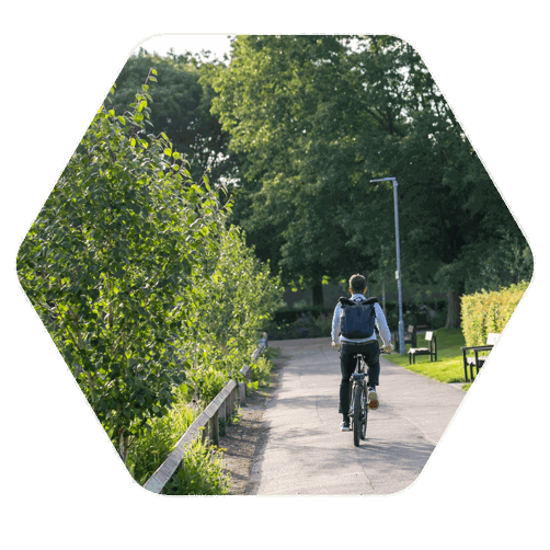 A man in work clothes, with a backpack on cycling through a park on the cycle path